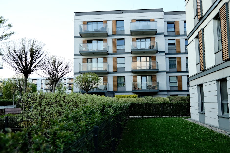 Contemporary apartment complex with balconies and lush garden in urban setting.