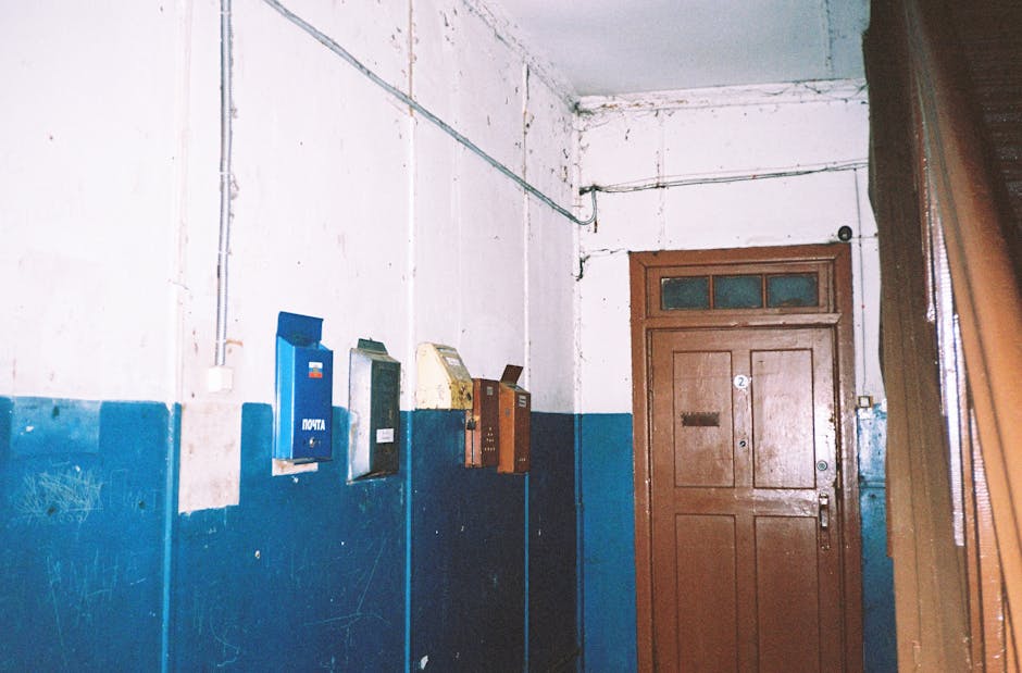 A rustic apartment hallway featuring old mailboxes and a wooden door.