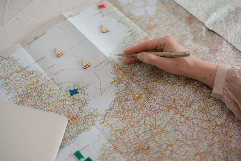 Hand holding pen over Europe map, planning travel route with markers.